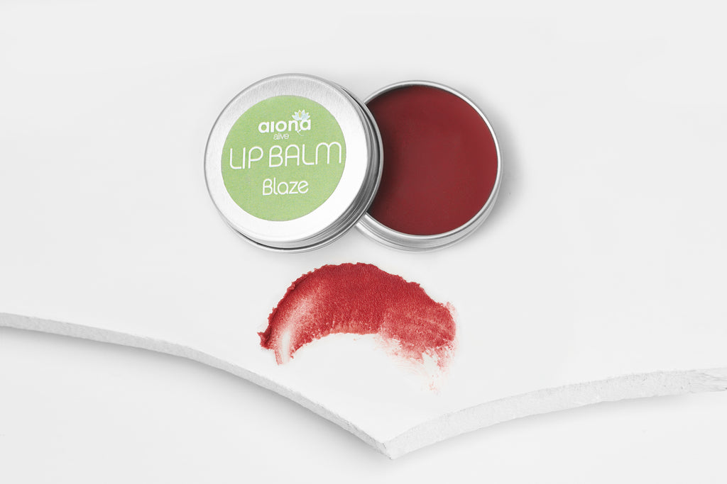Lip balm in a tin with a swatch of coral pink colour on a white background