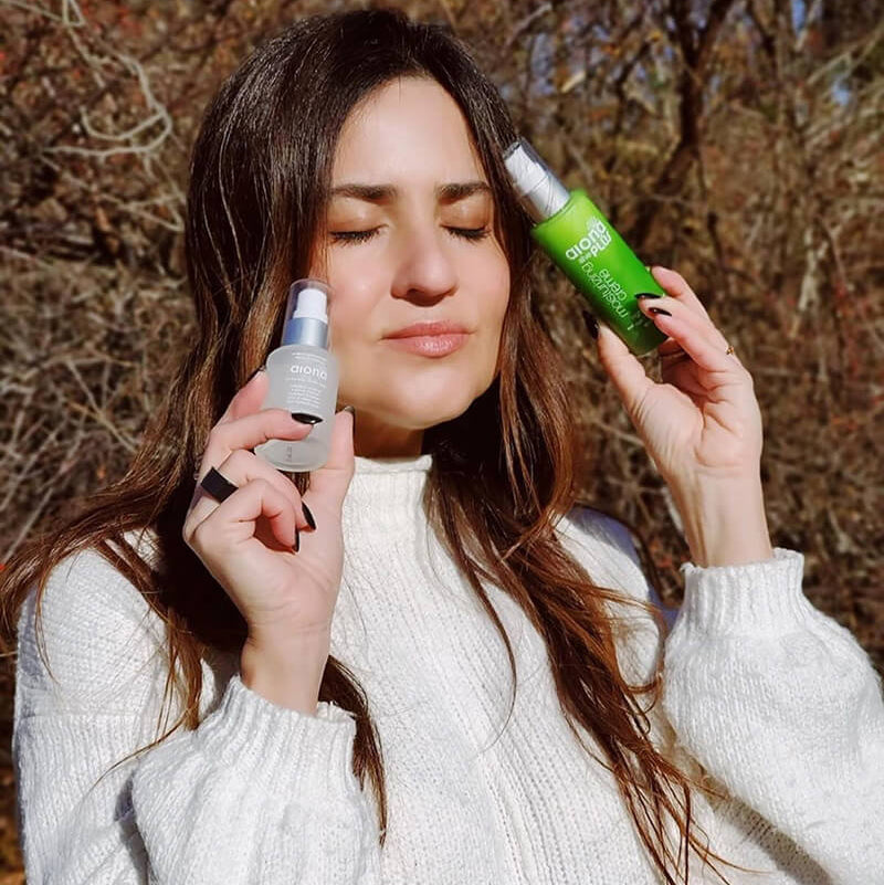 girl holding serums next to her face with green and clear bottle